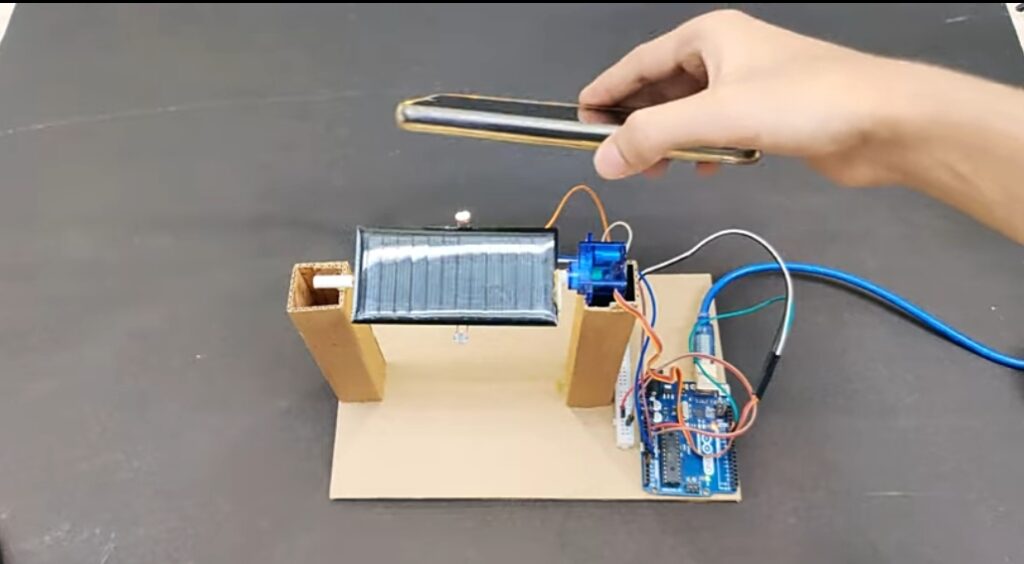  A working model of a solar tracking system, showing a solar panel connected to an Arduino, servo motor, and sensors, with a hand testing light direction.